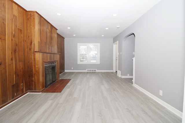 unfurnished living room featuring arched walkways, visible vents, a fireplace with flush hearth, light wood-type flooring, and baseboards