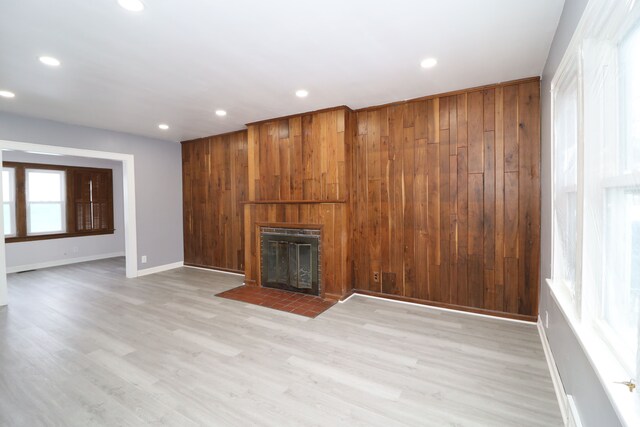 unfurnished living room with a fireplace with flush hearth, light wood-style floors, and wooden walls