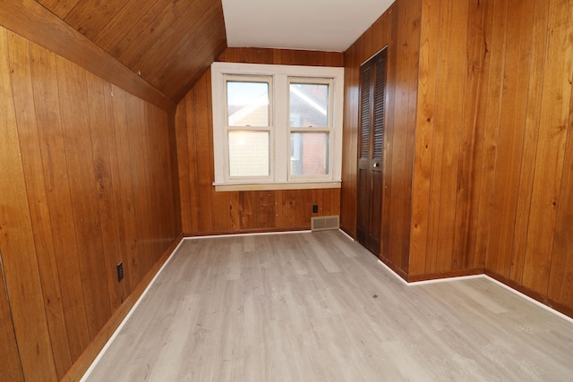 additional living space with wooden walls, visible vents, baseboards, vaulted ceiling, and light wood-type flooring