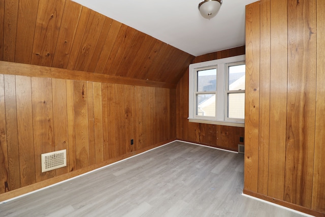 bonus room with lofted ceiling, visible vents, wooden walls, and light wood finished floors