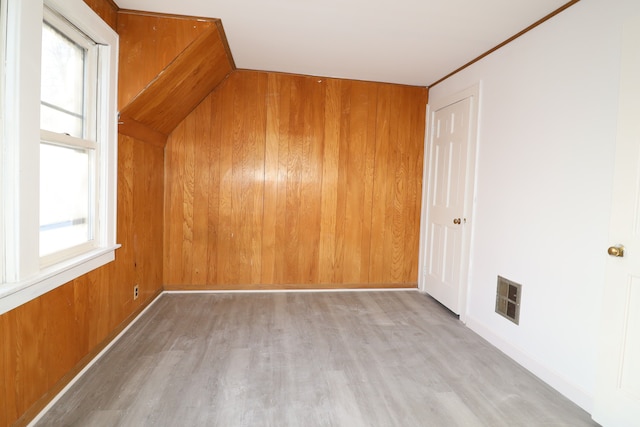 bonus room featuring light wood-style floors, wood walls, visible vents, and a healthy amount of sunlight