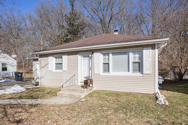 bungalow with roof with shingles, a chimney, and a front yard