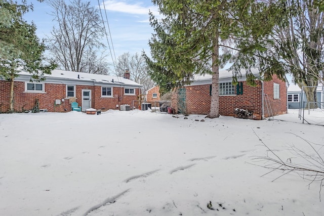 snow covered rear of property featuring a chimney, central AC unit, and brick siding