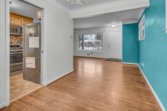 foyer entrance with baseboards, a notable chandelier, and light wood finished floors