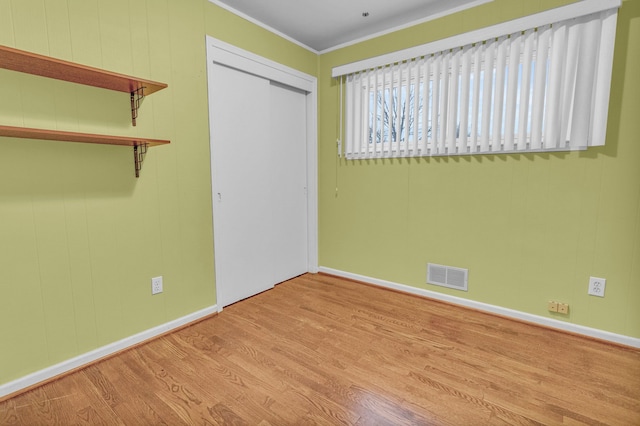 unfurnished bedroom with a closet, visible vents, light wood-style flooring, ornamental molding, and baseboards