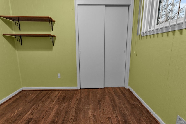 unfurnished bedroom with dark wood-style floors, baseboards, and a closet