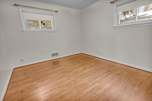 spare room with light wood-style floors, a wealth of natural light, and visible vents