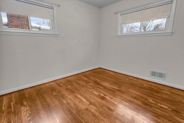 empty room with plenty of natural light, wood finished floors, visible vents, and baseboards