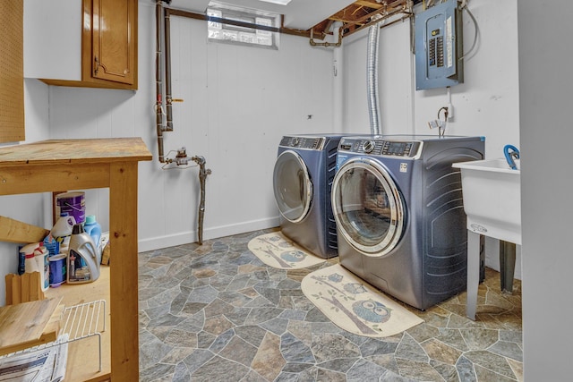 clothes washing area featuring a sink, cabinet space, electric panel, stone finish floor, and washing machine and clothes dryer