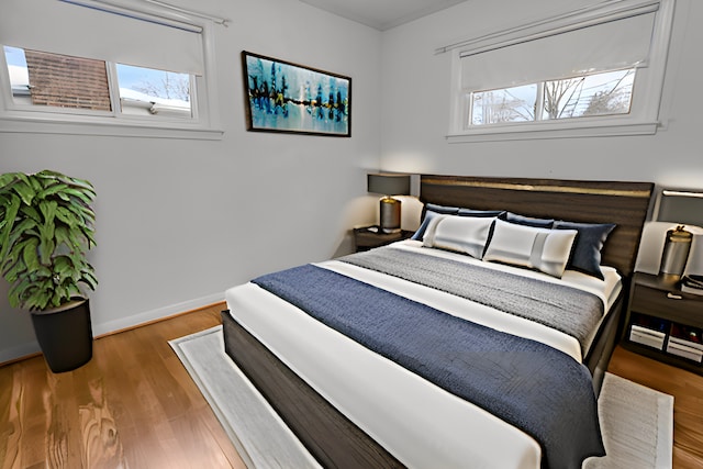 bedroom with multiple windows, wood finished floors, and baseboards