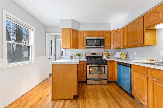 kitchen with a wainscoted wall, light countertops, appliances with stainless steel finishes, and light wood finished floors