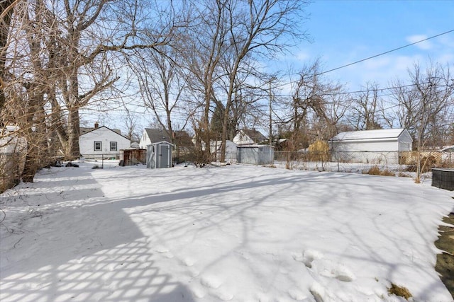 yard covered in snow featuring a storage shed, an outdoor structure, and fence