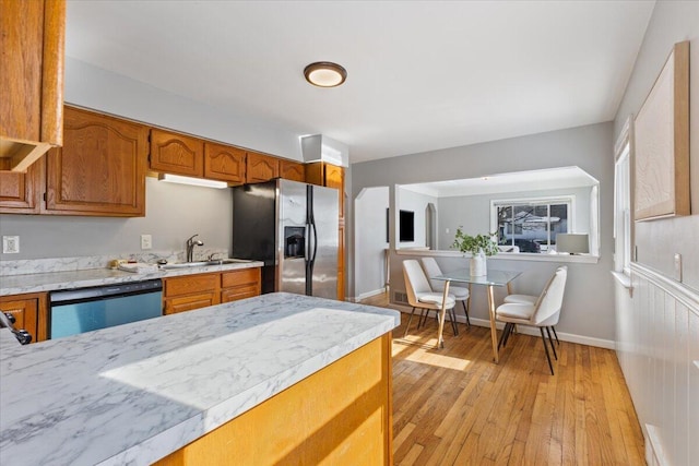 kitchen with a sink, stainless steel appliances, brown cabinetry, and light countertops