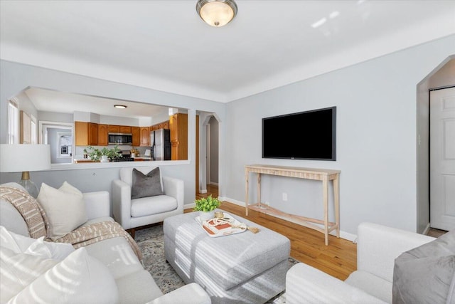 living area with arched walkways, light wood-style flooring, and baseboards