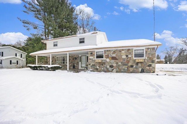 snow covered back of property featuring stone siding