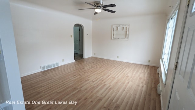 empty room with baseboards, visible vents, arched walkways, a ceiling fan, and light wood-style floors