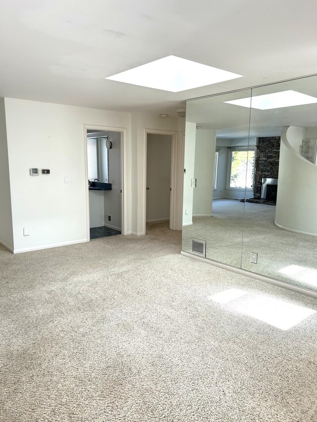 carpeted spare room with a skylight, visible vents, and baseboards