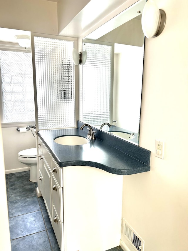 bathroom featuring toilet, vanity, visible vents, and baseboards