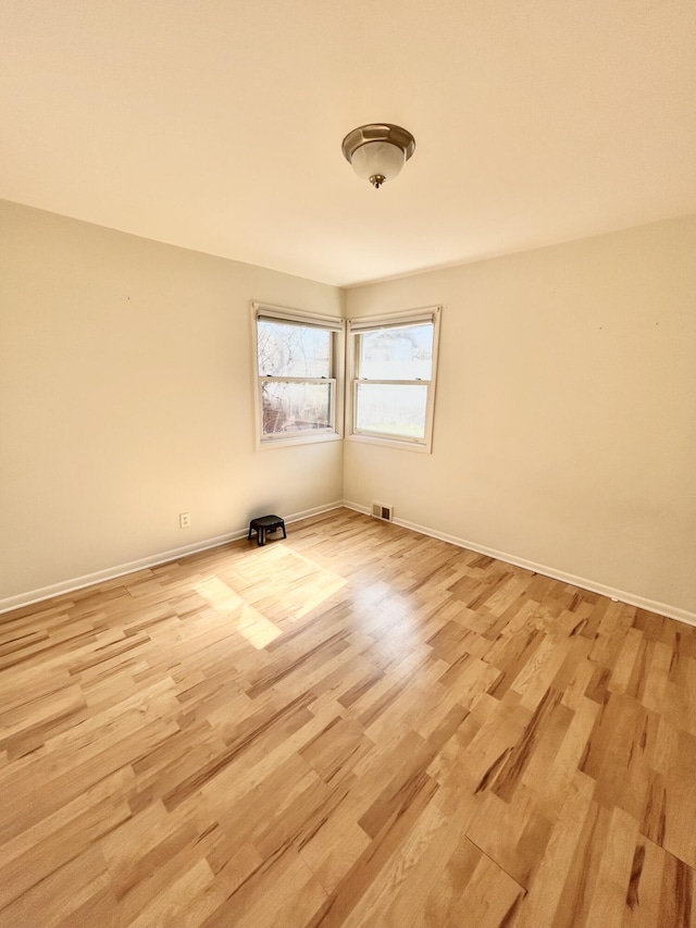 empty room featuring baseboards, visible vents, and light wood finished floors