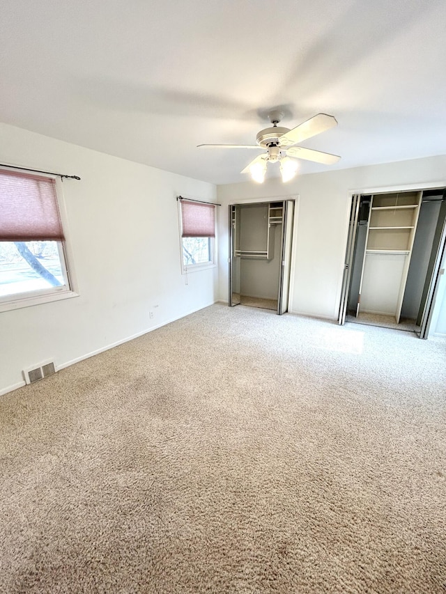 unfurnished bedroom with two closets, visible vents, a ceiling fan, carpet flooring, and baseboards