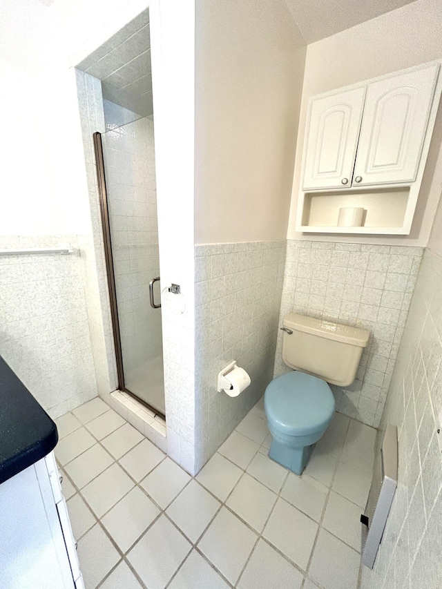 bathroom featuring tile patterned flooring, toilet, tile walls, wainscoting, and a stall shower