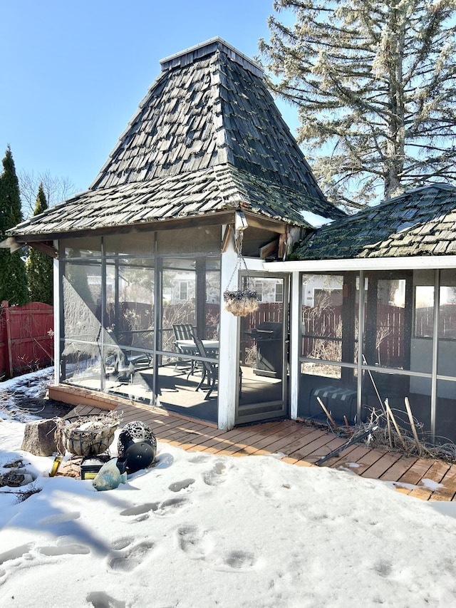 snow covered structure with a sunroom and fence