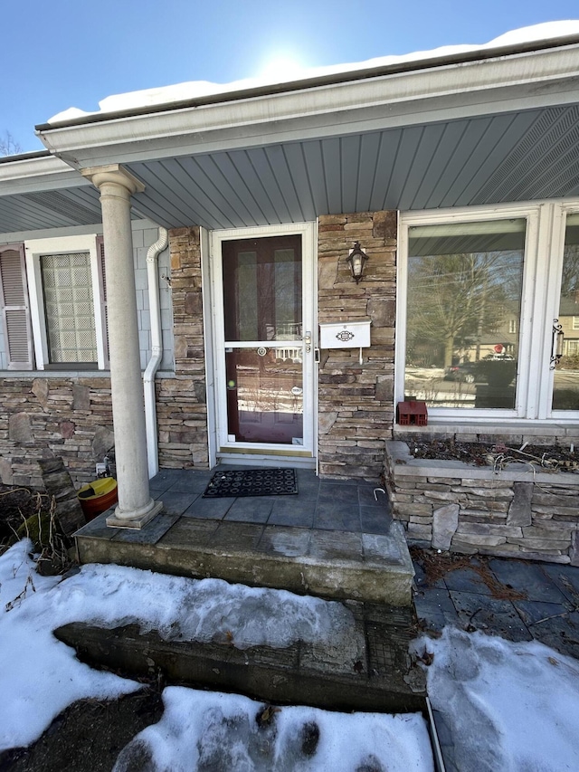 snow covered property entrance featuring stone siding