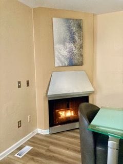 interior details with baseboards, wood finished floors, visible vents, and a lit fireplace