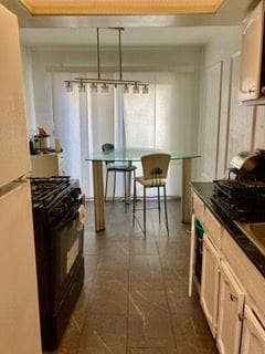 kitchen featuring a raised ceiling, dark countertops, gas stove, and freestanding refrigerator