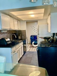 kitchen featuring a sink, backsplash, dark countertops, white cabinetry, and freestanding refrigerator