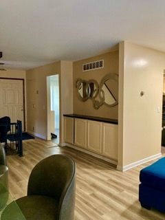 living room with light wood-type flooring, visible vents, and baseboards