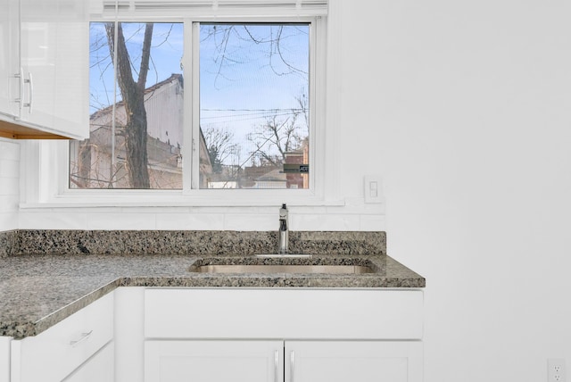 room details featuring dark stone countertops, white cabinetry, and a sink