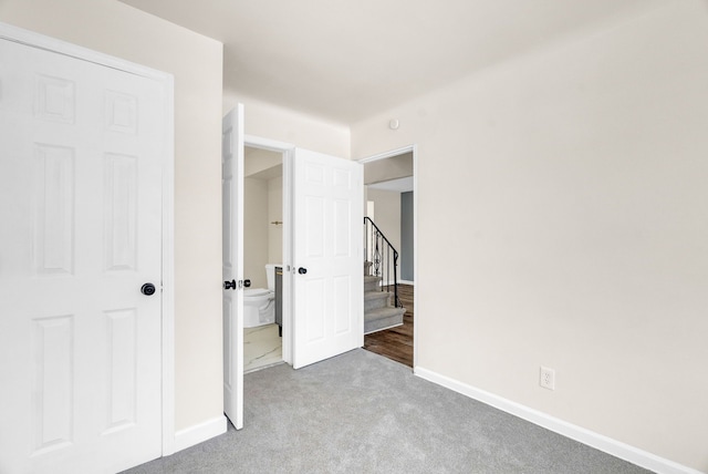 unfurnished bedroom featuring light carpet, ensuite bathroom, and baseboards