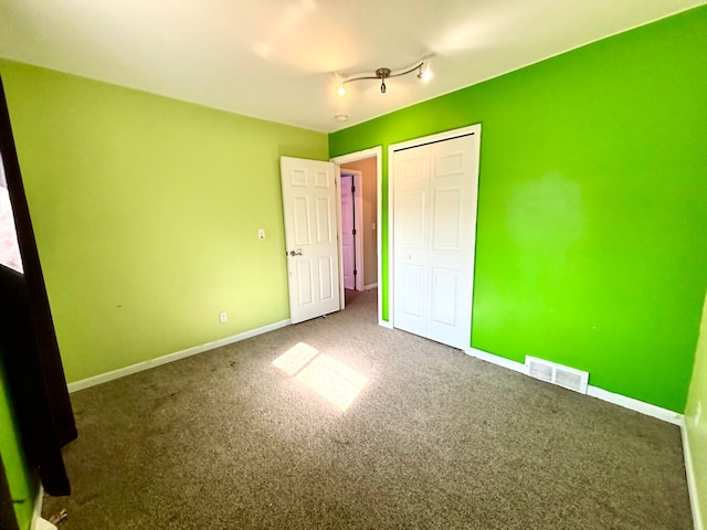 unfurnished bedroom featuring a closet, baseboards, visible vents, carpet, and track lighting