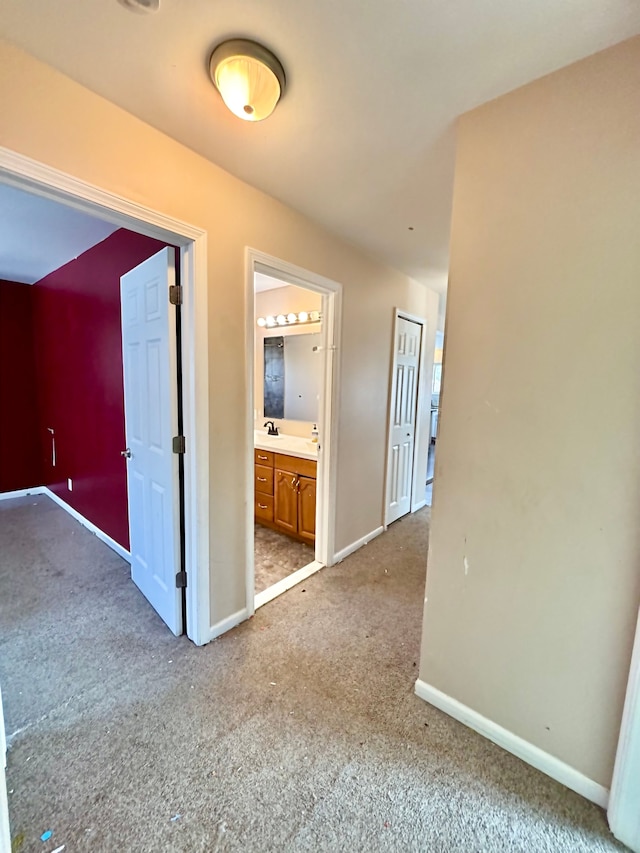 hallway featuring carpet, a sink, and baseboards