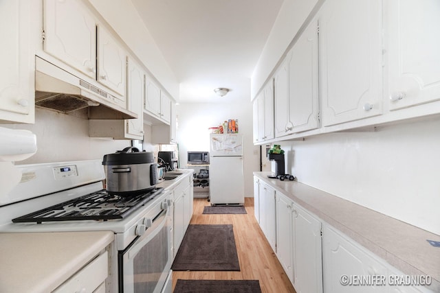 kitchen with under cabinet range hood, white appliances, white cabinetry, light countertops, and light wood finished floors