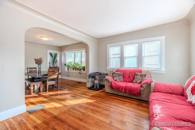 living area with baseboards, visible vents, arched walkways, and hardwood / wood-style floors