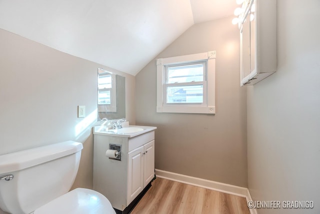 half bath with toilet, wood finished floors, vanity, baseboards, and vaulted ceiling