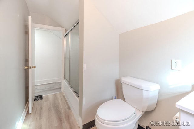 bathroom featuring toilet, wood finished floors, vanity, vaulted ceiling, and combined bath / shower with glass door