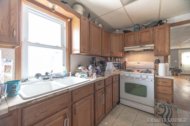 kitchen with under cabinet range hood, white range with gas stovetop, light countertops, and a sink