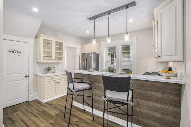 kitchen with glass insert cabinets, freestanding refrigerator, dark wood-type flooring, a peninsula, and a kitchen bar