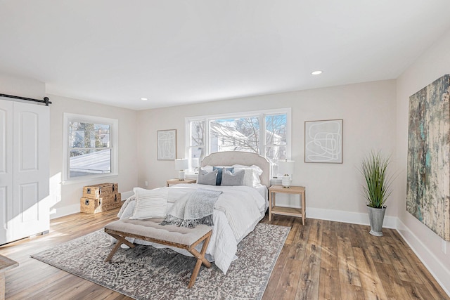 bedroom with recessed lighting, wood-type flooring, baseboards, and a barn door