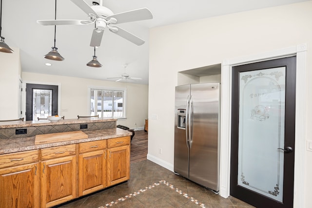 kitchen with dark tile patterned flooring, baseboards, stainless steel fridge with ice dispenser, brown cabinetry, and decorative light fixtures