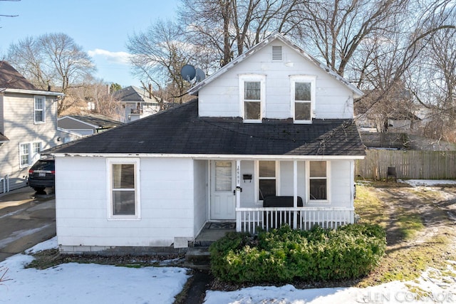 view of front facade featuring covered porch, roof with shingles, and fence