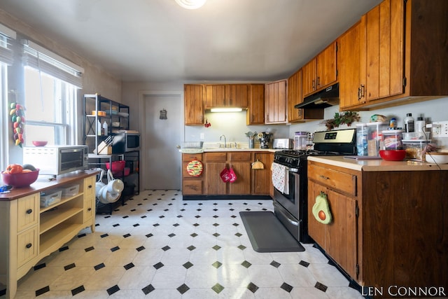 kitchen with brown cabinets, light floors, light countertops, gas range, and under cabinet range hood