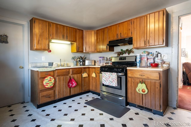 kitchen with light countertops, brown cabinetry, a sink, under cabinet range hood, and stainless steel gas range oven