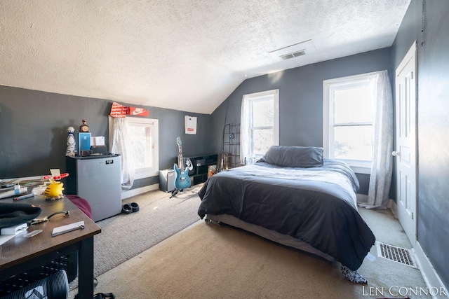 bedroom featuring lofted ceiling, a textured ceiling, light carpet, visible vents, and freestanding refrigerator