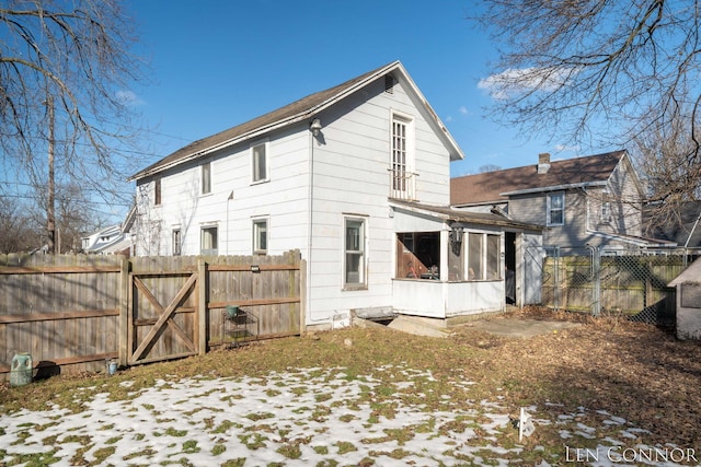 snow covered rear of property featuring a sunroom, a gate, and fence