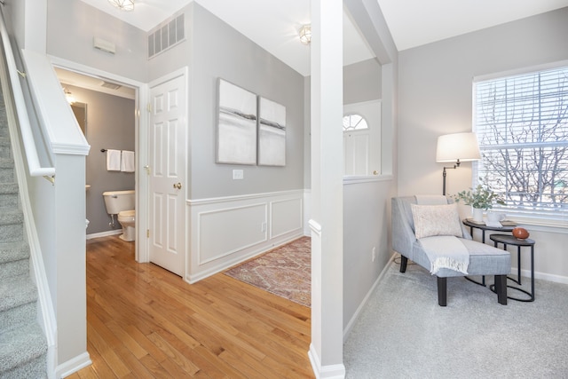 sitting room featuring a wainscoted wall, visible vents, a decorative wall, light wood-style floors, and stairs