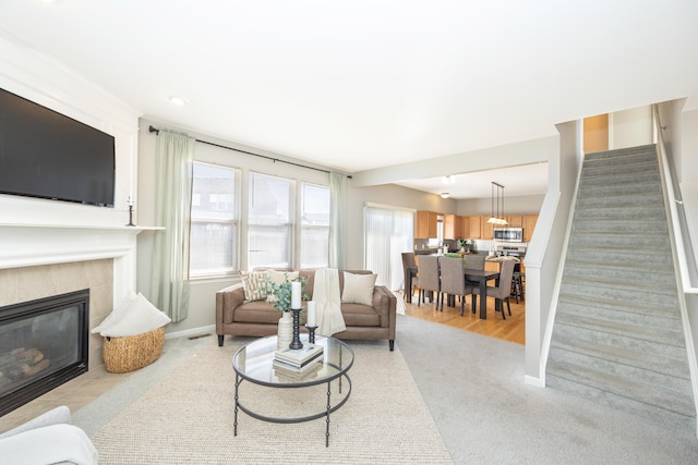 living area featuring a tile fireplace, visible vents, baseboards, and stairs